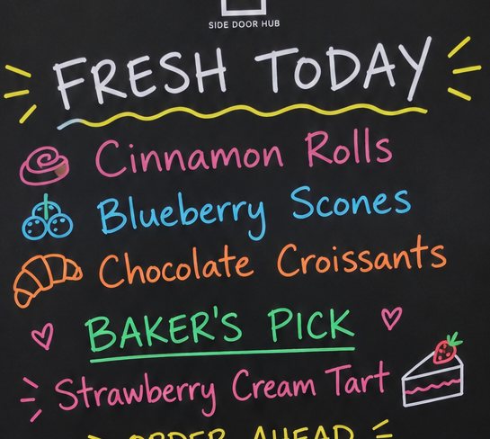 The writable area of a Side Door Hub board in a bakery: “Fresh today — cinnamon rolls, blueberry scones, chocolate croissants,” plus the baker’s pick.
