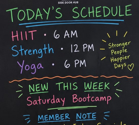 The writable area of a Side Door Hub board in a fitness studio listing today’s class schedule.